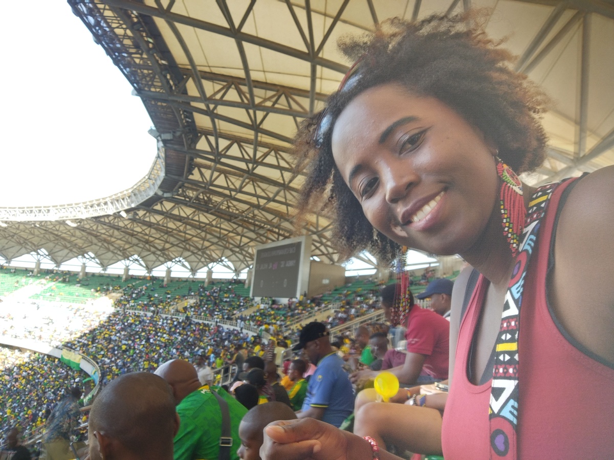 Sarah smiling with the crowd at Benjamin Mkapa Stadium in Dar es Salaam, Tanzania during a Young Africans SC football match.
