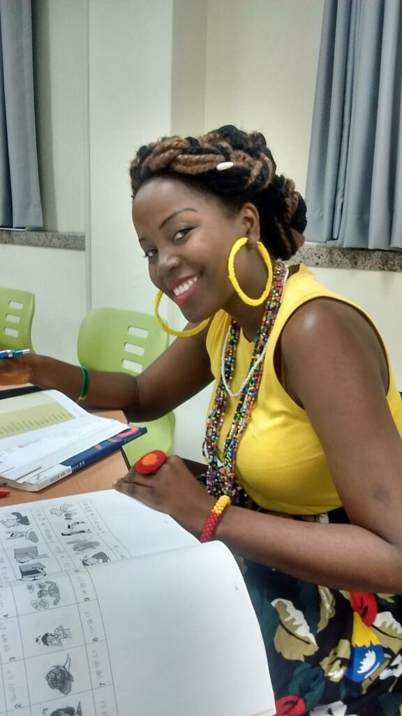 Sarah smiling while sitting at a desk and practicing writing Korean characters in a notebook.