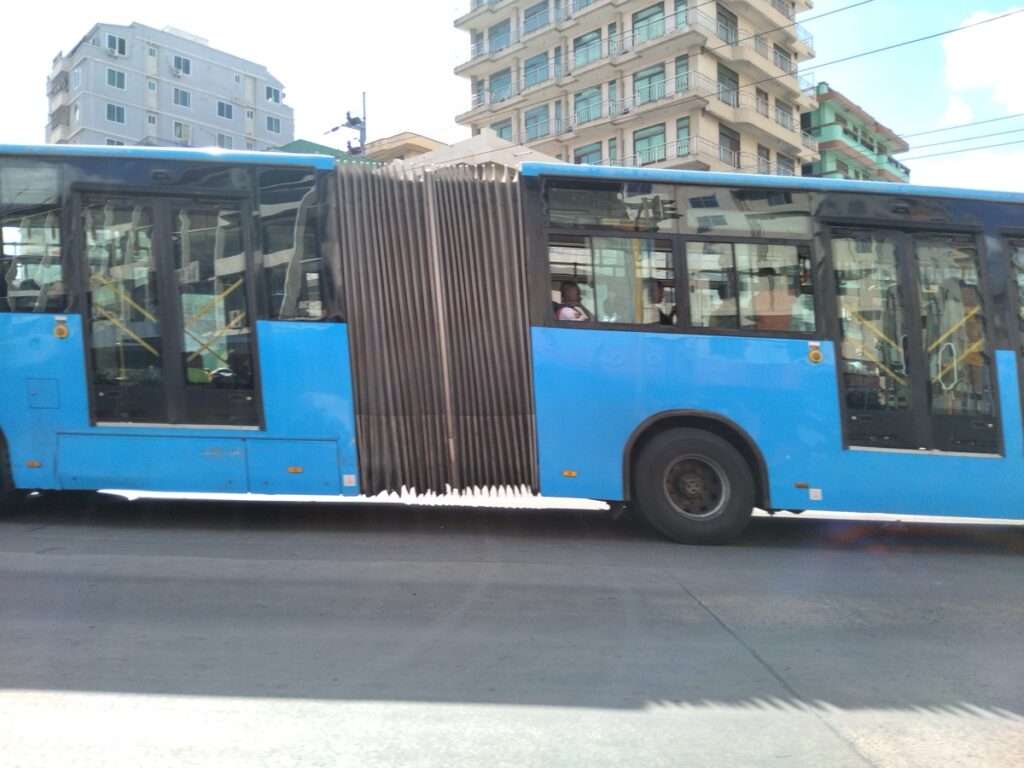 Blue city bus carrying football supporters through the busy streets of Dar es Salaam, Tanzania.
