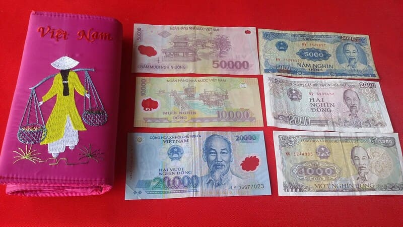 A wallet open on a flat surface displaying several colorful Vietnamese Dong banknotes.