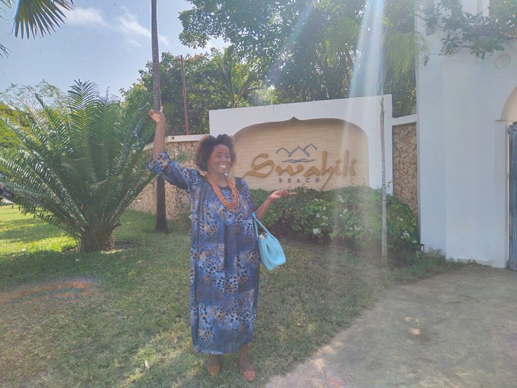 Sarah smiling in front of the grand, arched wooden entrance of the Swahili Beach Resort in Diani Beach.